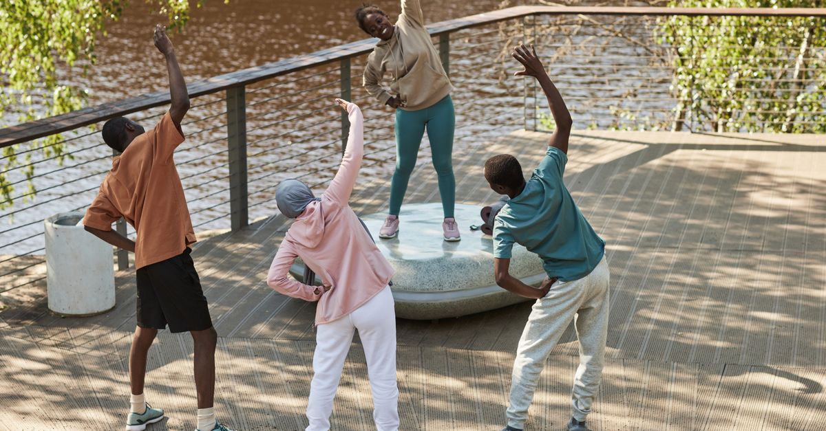 Four adults stretch and exercise outdoors near a riverside park, enjoying a healthy lifestyle.
